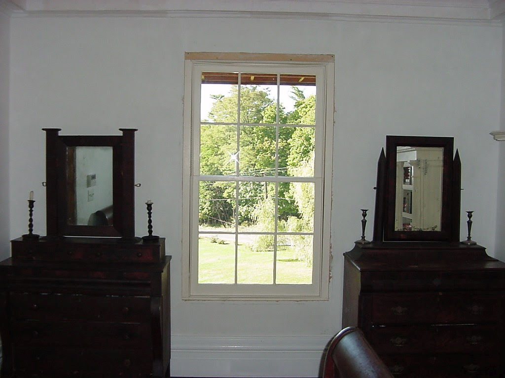 Bedroom with two mahogany dressers flanking a hand-made window, summer lawn beyond